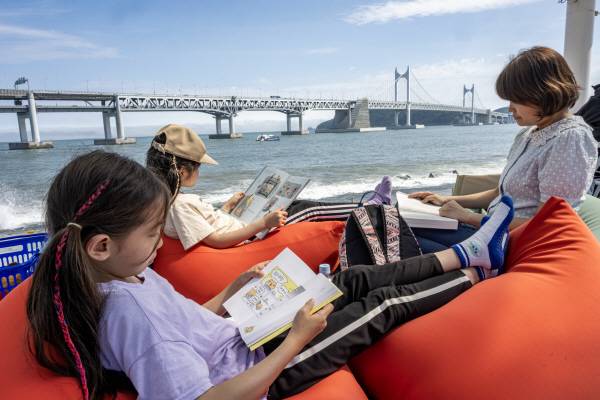 지난 6월 부산 수영구 민락수변공원 일원에서 ‘2025 부산바다도서관’이 열려 시민이 그늘 아래서 시원하게 독서를 하고 있다. 국제신문DB