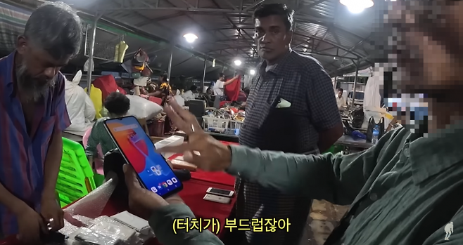 미얀마 양곤 여행을 간 여행유튜버 제여비가 마하반둘라 공원에서 우연히 만난 현지인 남성(오른쪽)이 중고 휴대전화를 고르며 마음에 들어 하고 있다(사진 일부 모자이크 처리함). 유튜브 채널 ‘제여비’ 캡처