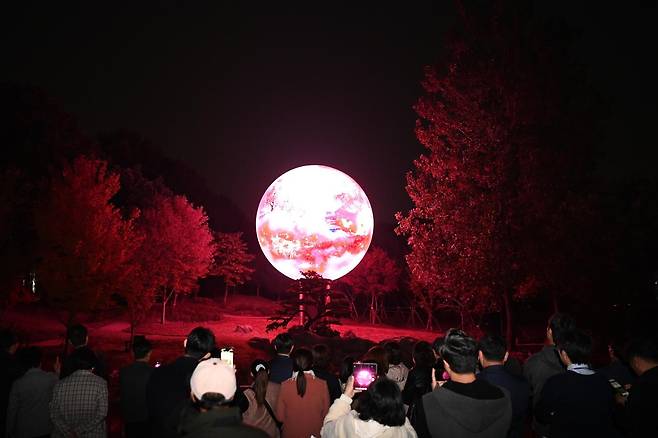 부천자연생태공원에 조성된 ‘루미나래’를 찾은 시민들이 ‘달밤’ 구간의 미디어아트 조형물을 휴대전화로 촬영하고 있다. 연못 위에 떠 있는 달을 형상화한 작품이다. 부천시 제공