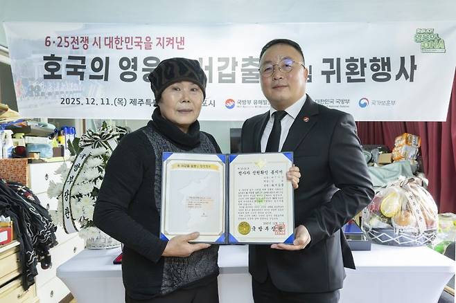 고 서갑출 일병의 며느리인 이정순 씨(72세, 왼쪽)와 조해학 국방부유해발굴감식단장 직무대리(육군 중령, 오른쪽)가 함께 전사자 신원확인 통지서를 들고 기념사진을 촬영하고 있다.