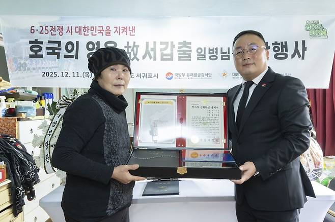 고 서갑출 일병의 며느리인 이정순 씨(72세, 왼쪽)와 조해학 국방부유해발굴감식단장 직무대리(육군 중령, 오른쪽)가 함께 호국의 얼 함을 들고 기념사진을 촬영하고 있다.