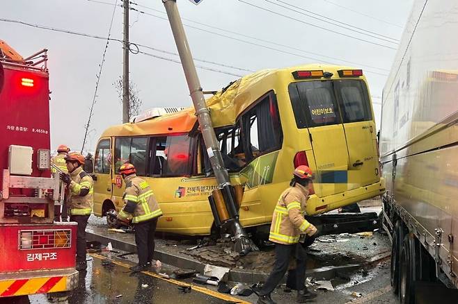 지난 23일 오후 4시26분쯤 전북 김제시 백산면 상정리 지평선산단로 돌제교차로에서 초등학교 스쿨버스가 화물 윙바디 트럭과 충돌한 뒤 안전지대에 세워진 신호등과 추돌하는 사고가 나자 119 구급대원들이 분주하게 움직이고 있다. 전북도소방본부 제공