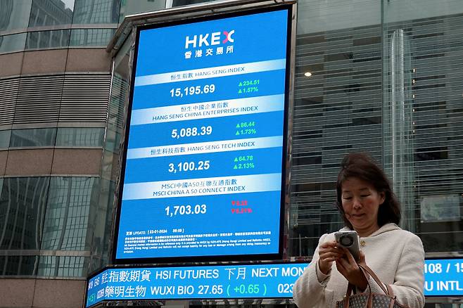 중국 홍콩 증권거래소 광장 밖에서 한 여성이 항셍지수와 주가를 보여주는 전광판 근처에서 휴대전화를 확인하고 있다. /연합뉴스