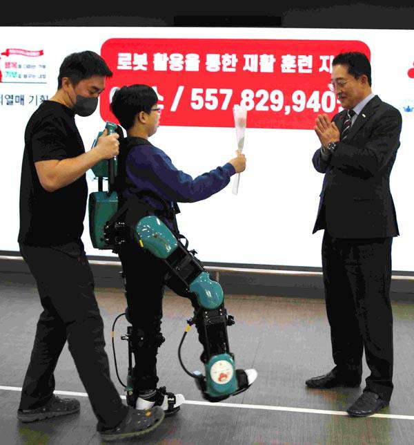 로봇에 의지해 재활치료를 받고 있는 이준서(가운데) 군이 이수태 부산사랑의열매 회장에게 장미꽃을 전달하고 있다. 사랑의열매 제공