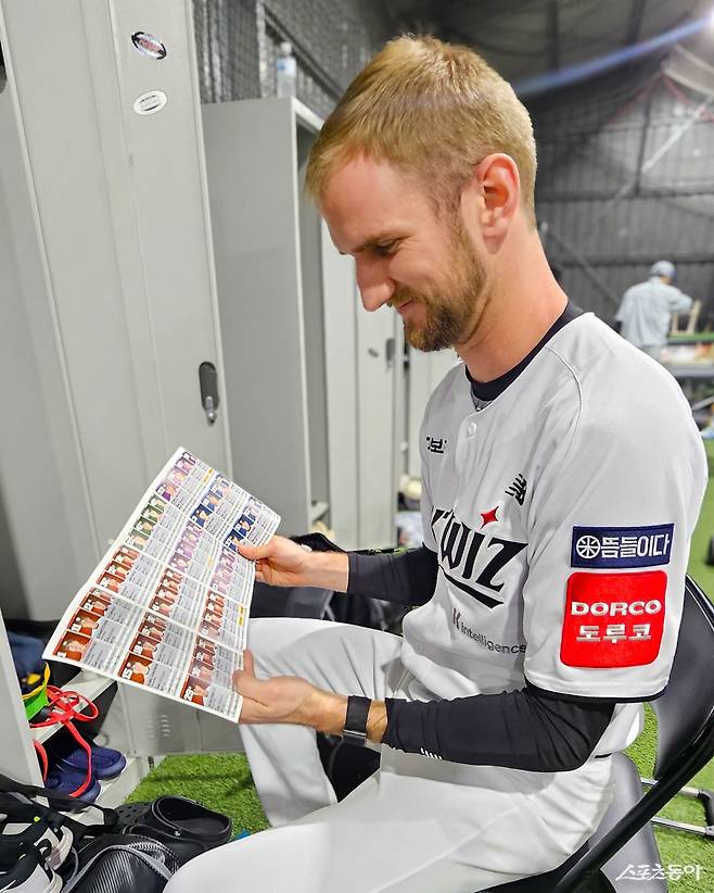 KT 외국인 투수 케일럽 보쉴리가 26일 호주 질롱 베이스볼 센터의 라커룸에 앉아 구단 커뮤니케이션팀 주도로 제작한 선수단 안내 팸플릿을 보고 있다. 함나얀 커뮤니케이션팀 대리, 정민주 마케팅기획팀 매니저가 매년 팸플릿을 직접 기획하고 제작해 한국야구를 알리고 있다. 사진제공|KT 위즈