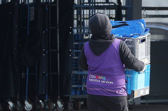 쿠팡의 배송 전문 자회사인 쿠팡로지스틱스 서비스 조끼를 입은 한 노동자가 지난 1월 23일 서울의 한 쿠팡 물류센터에서 상자를 옮기고 있다. 연합뉴스