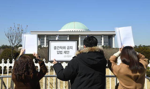 한국일보 마이너리티팀 기자들이 지난 2021년 2월 서울 여의도에서 국회를 바라보며 '중간착취 금지 입법 제안' 손팻말과 국회의원들에게 전달할 질의서를 들고 있다. 한국일보 자료사진