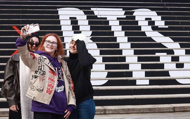 11일 서울 종로구 세종문화회관 계단에서 러시아 관광객들이 '완전체'로 돌아오는 그룹 방탄소년단(BTS) 공연 홍보물을 배경으로 기념촬영을 하고 있다. 연합뉴스
