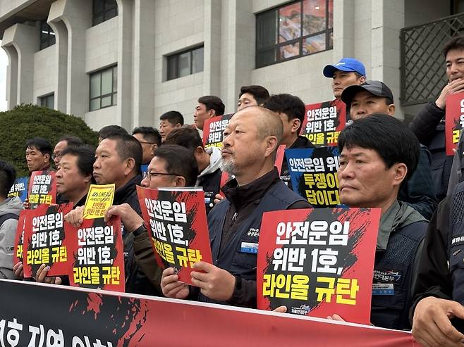 ▲ 화물연대본부 조합원들이 6일 오전 인천시청 앞에서 '안전운임 위반 1호, 라인올 규탄'이라고 적힌 피켓을 들고 기자회견을 하고 있다.