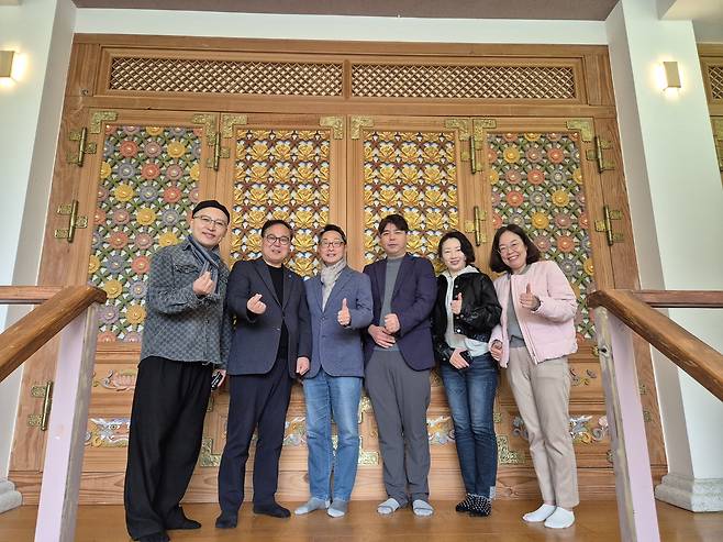 FAMS 2026 운영진이 금선사 내부 건물 중 무궁화꽃과 연꽃이 새겨진 출입문 문양 앞에서 포즈를 취하고 있다.