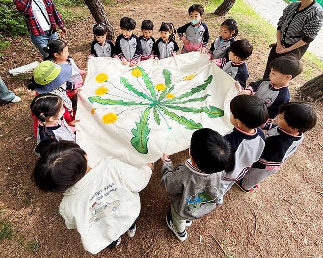 봄 숲속에서 유아들이 숲해설가의 설명을 듣고 꽃과 식물을 배우고 있다(사진=제천교육지원청 제공)