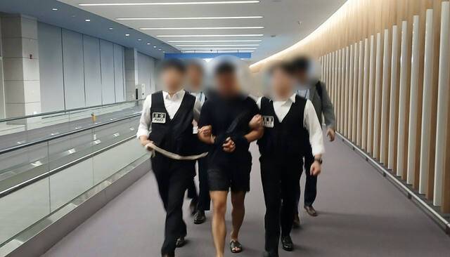 법무부 관계자들이 그룹 방탄소년단(BTS) 정국을 포함한 국내 재력가들의 명의를 도용해 거액을 빼돌린 해킹조직 총책급 범죄인인 중국 국적 전모(34)씨를 인천국제공항을 통해 강제송환하고 있다. 연합뉴스