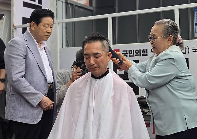 부산 북갑에 출마한 박민식 국민의힘 후보가 21일 부산 북구 구포시장 쌈지공원에서 출정식을 갖고 삭발을 하는 모습, 오른쪽은 박 후보의 어머니다 / 뉴스1