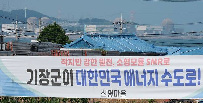 한국수력원자력이 신규 원전 건설을 위한 후보 부지로 대형원전 2기는 경북 영덕군, SMR 1기는 기장군을 확정했다고 밝힌 가운데 18일 부산 기장군 신평마을회관 인근 도로변에 내걸린 SMR 기장군 유치를 희망하는 내용의 현수막 뒤로 고리 1, 2, 3, 4호기가 보인다. 연합뉴스.