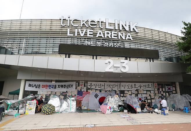 지난달 27일 6·3 지방선거 투표소 봉쇄 시위가 이어지고 있는 서울 송파구 올림픽공원 핸드볼경기장 입구 근처에서 시민들이 앉아 있다. 연합뉴스