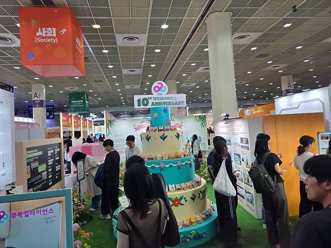행복얼라이언스 10주년 부스에 설치된 대형 케이크 조형물 주변에서 관람객들이 전시를 둘러보는 모습. ⓒ데일리안 정진주 기자