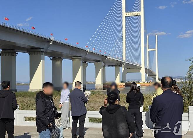 신압록강대교 정식 개통을 하루 앞둔 14일 중국 랴오닝성 단둥의 대교 인근에 관광객들이 모여 있다. 뒤로 보이는 대교 중국 측 구간에는 오성홍기가 줄지어 내걸려 있다. 2026.10.14. ⓒ 단둥=뉴스1 노민호 특파원
