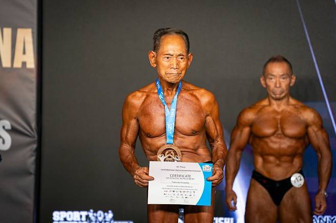 90세 日 보디빌더, 세계선수권 대회 6위 - 90세 보디빌더 가나자와 도시스케(일본)가 30일(현지 시간) 스페인 산타수산나에서 열린 2026 국제보디빌딩·피트니스연맹(IFBB) 세계 피트니스·보디빌딩 선수권대회에 출전해 6위 증서를 들어 보이고 있다. 가나자와는 “목표는 우승이 아니라 몇 살까지 계속 출전할 수 있느냐는 것”이라며 95세까지는 출전을 이어가고 싶다고 밝힌 바 있다. 2026.10.31. AP뉴시스